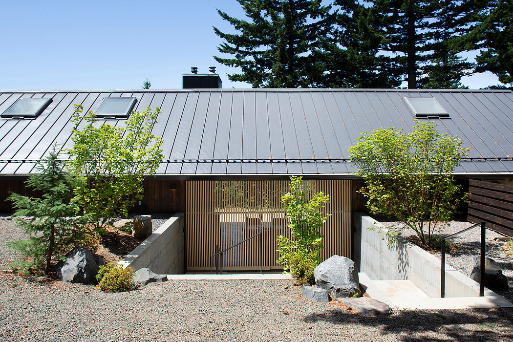 A contemporary building with a metal roof, wooden siding, and a gravel courtyard surrounded by trees.