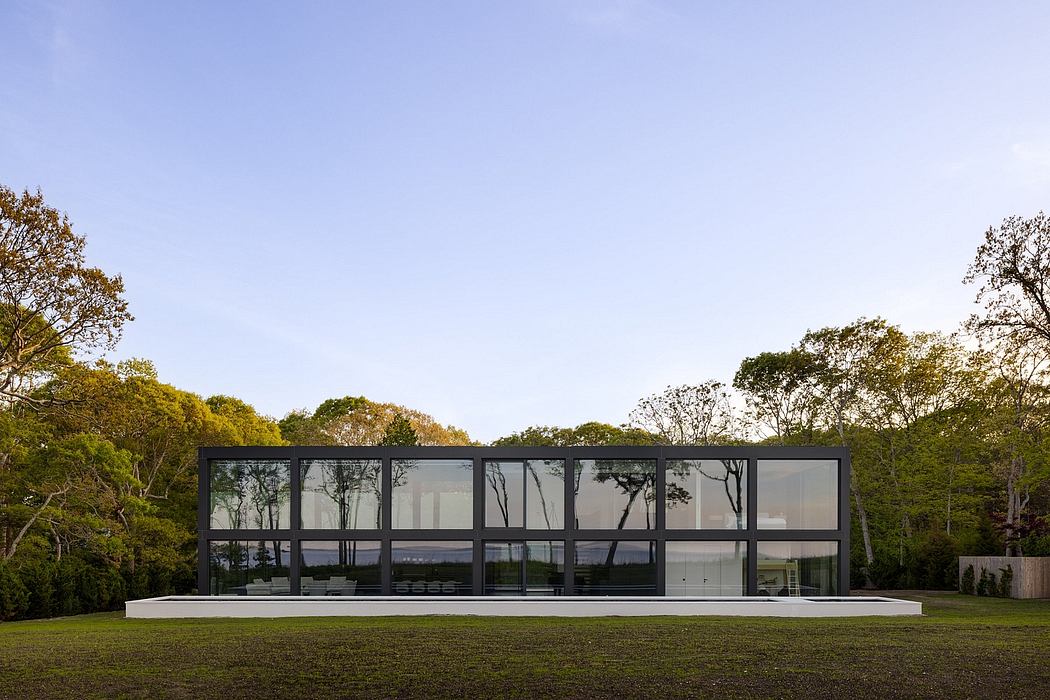 A modern glass pavilion nestled in a lush, wooded landscape with expansive views.