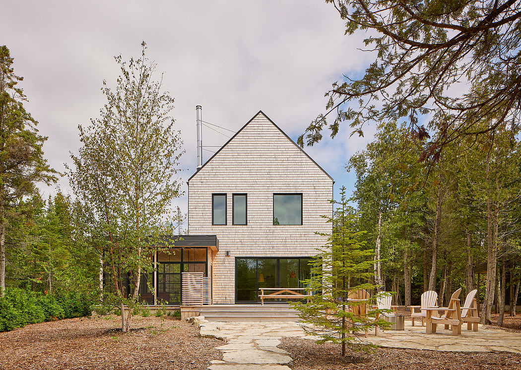 A modern, gabled-roof house nestled in a forested setting with an inviting outdoor patio.