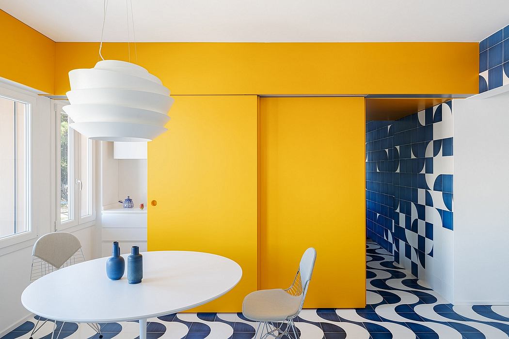 Vibrant yellow walls, patterned blue tiles, and a minimalist white dining set create a bold, modern aesthetic.