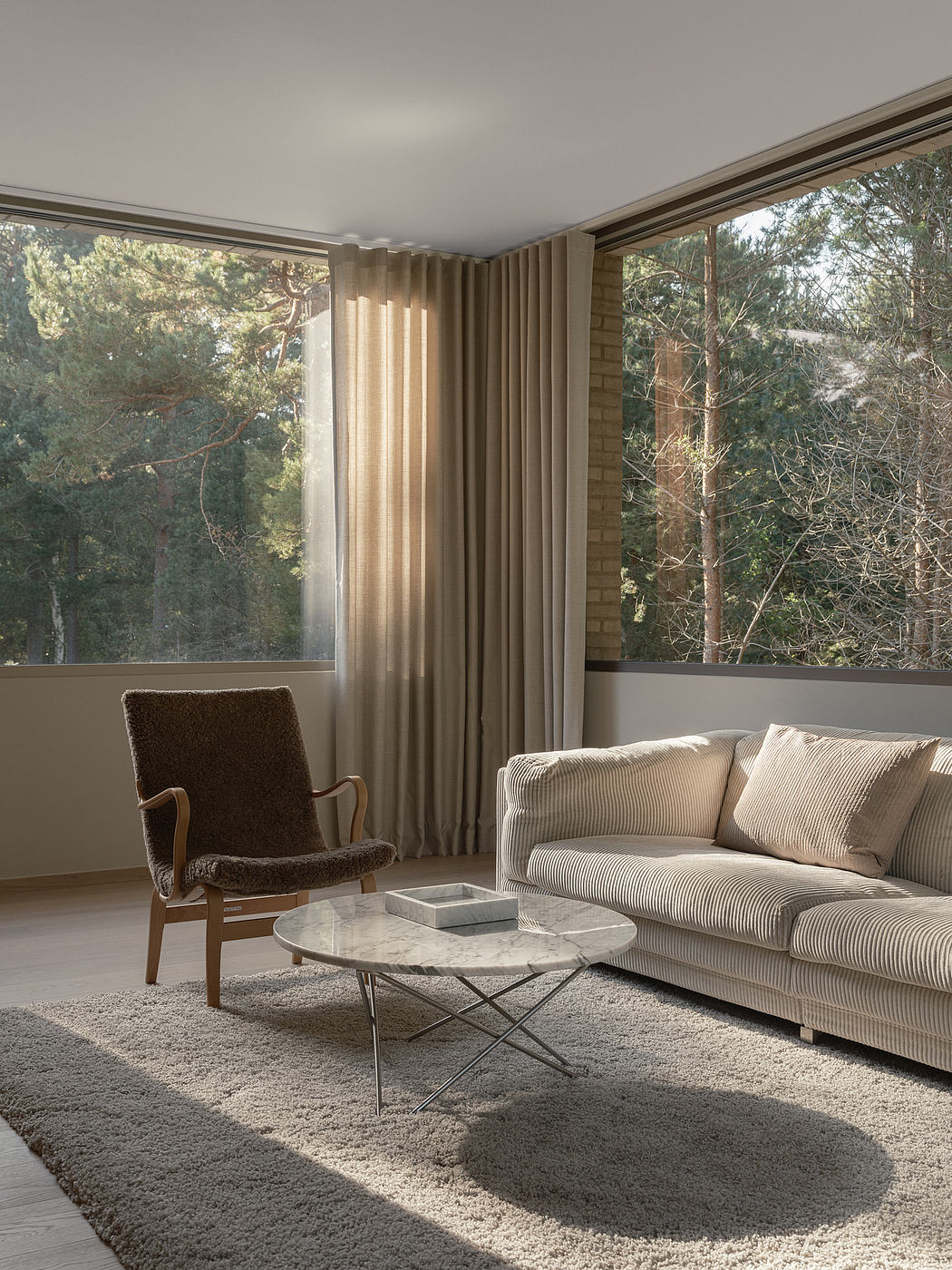 A cozy living room with floor-to-ceiling windows, plush furnishings, and a marble coffee table.