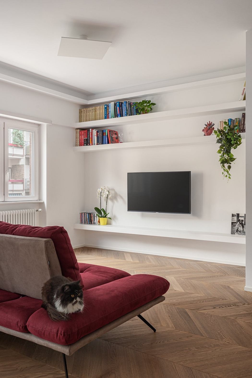 Cozy living room with built-in shelving, TV, and plush red sofa in modern design.