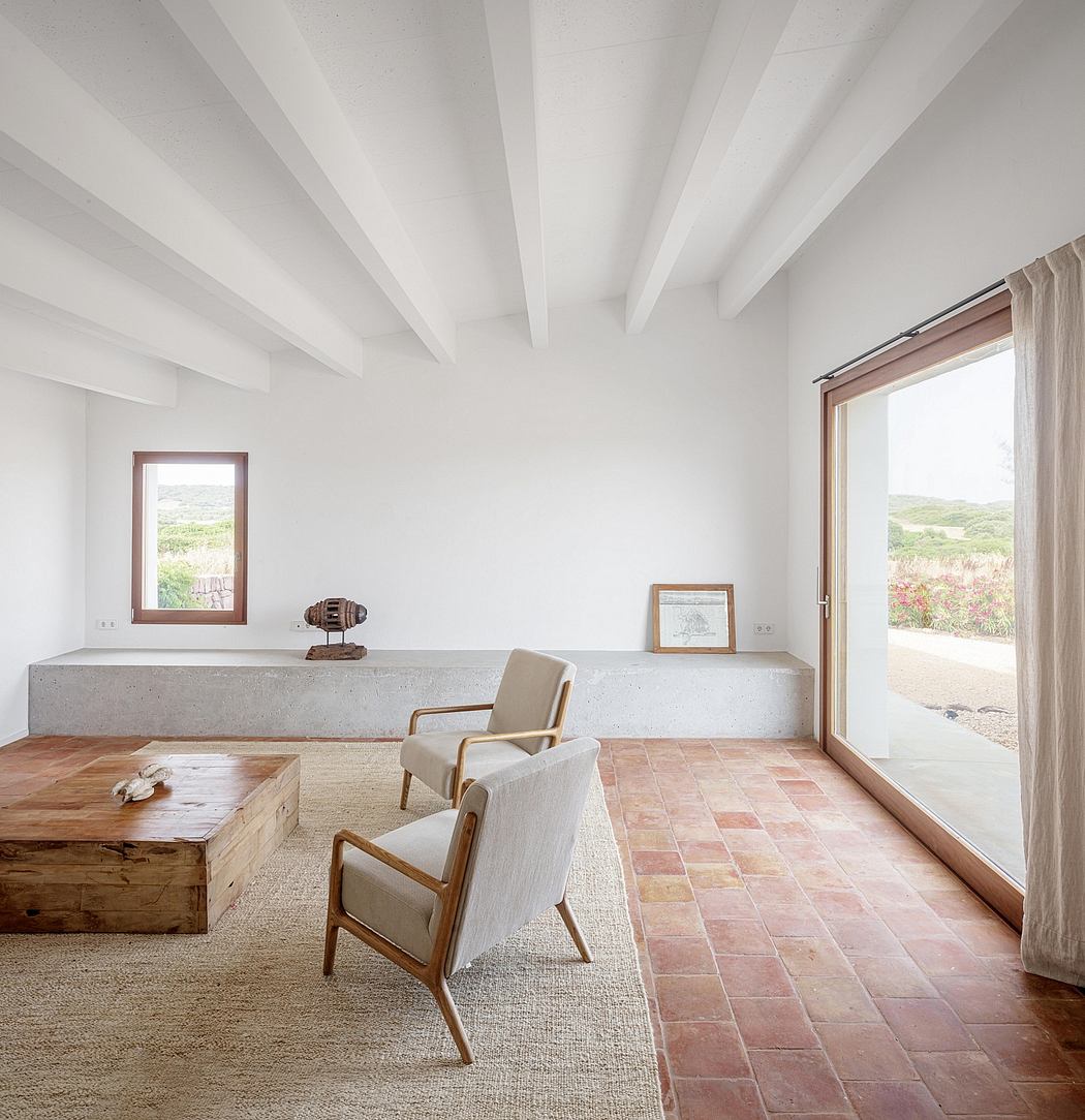 A minimalist living room with exposed beams, concrete surfaces, and terracotta floors.