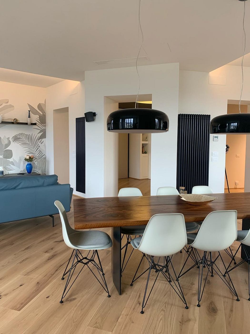 Modern dining area with a large wooden table, white chairs, and a stylish black pendant light.