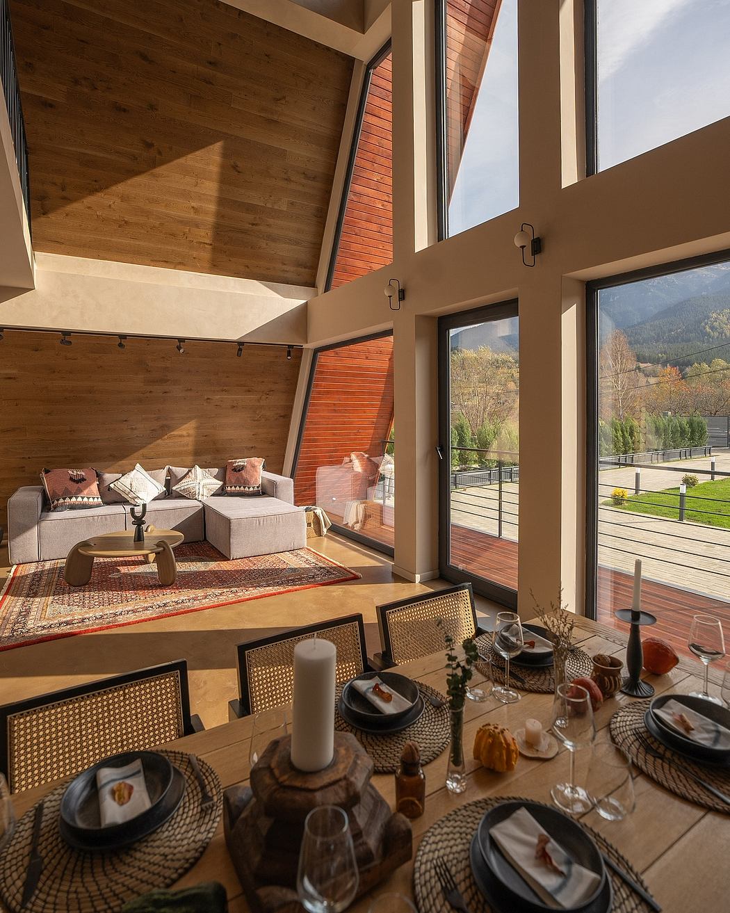 A cozy mountain cabin interior with wooden beams, large windows overlooking the scenery, and a stylish dining area.