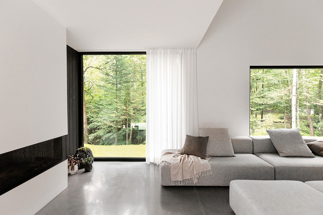 Minimalist living room with large windows overlooking a lush forest landscape.