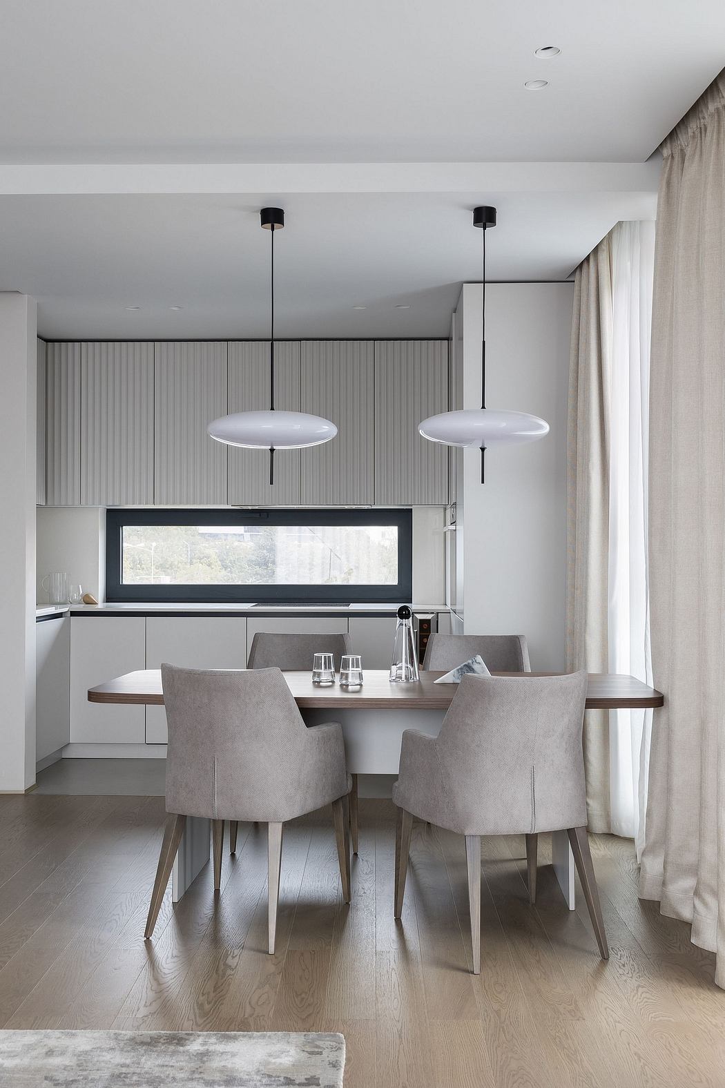 Modern, minimalist kitchen with sleek gray cabinets, pendant lighting, and a wooden dining table.