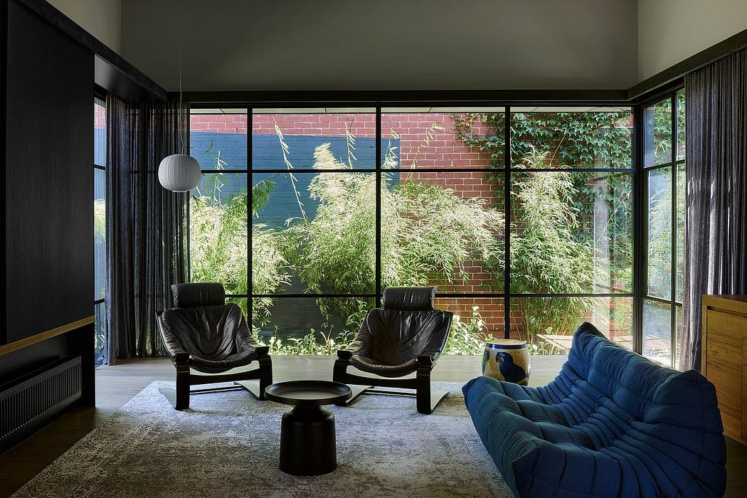 A modern living room with large windows overlooking lush greenery, dark furnishings, and a cozy ambiance.