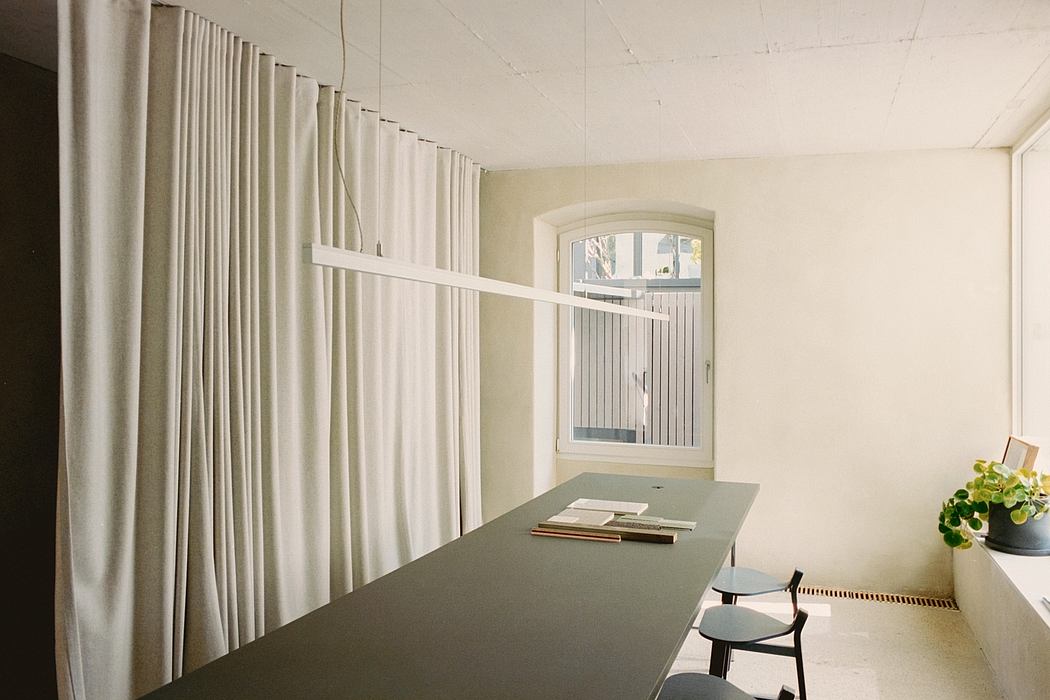 Clean, minimalist room with floor-to-ceiling curtains, wooden table, and arched window.