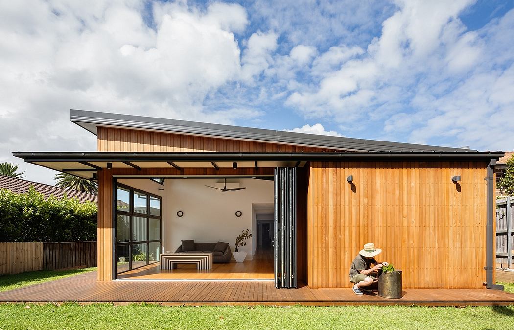 Modern wooden structure with covered patio and sliding glass doors, surrounded by lush greenery.