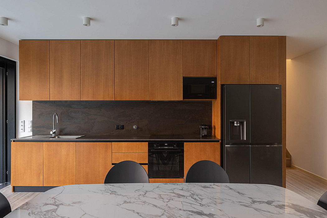 Sleek, modern kitchen with wood cabinetry, marble countertop, and black appliances.