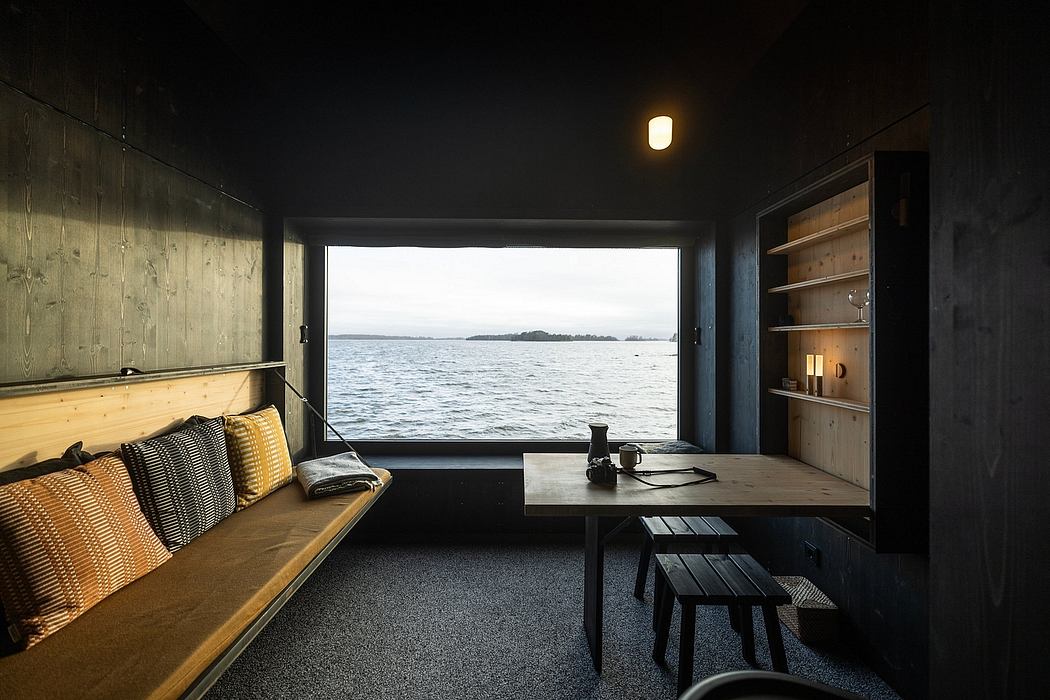 Cozy cabin interior with wooden furniture and stunning water view through large window.