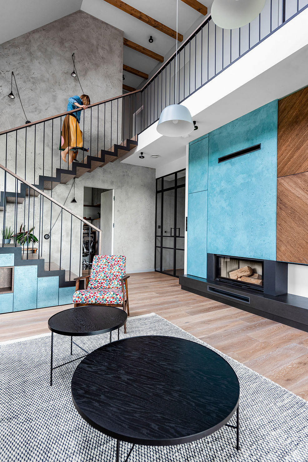 Modern living room with concrete walls, wood beams, colorful furniture, and sleek fireplace.