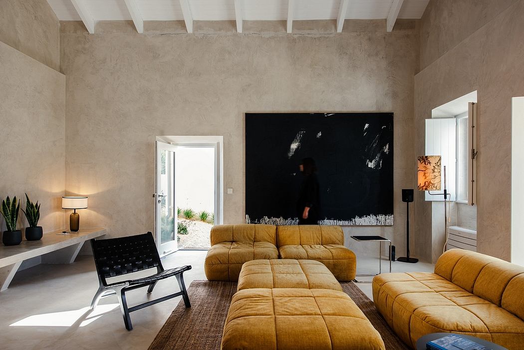 Minimalist living room with exposed concrete walls, warm-toned upholstered furniture, and a large black artwork.