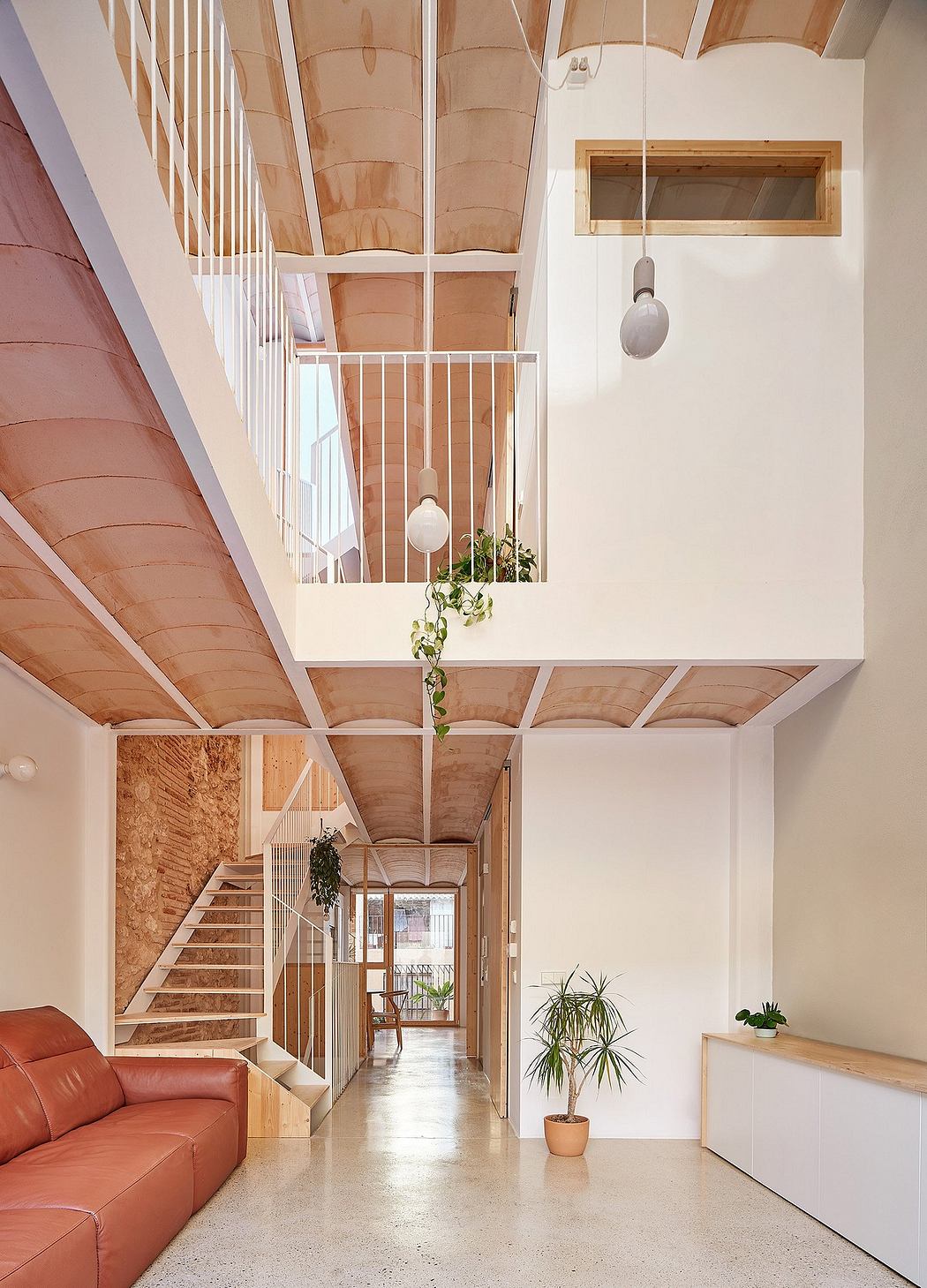 Spacious open-concept interior with wooden beams, a red sofa, and a plant-filled hallway.