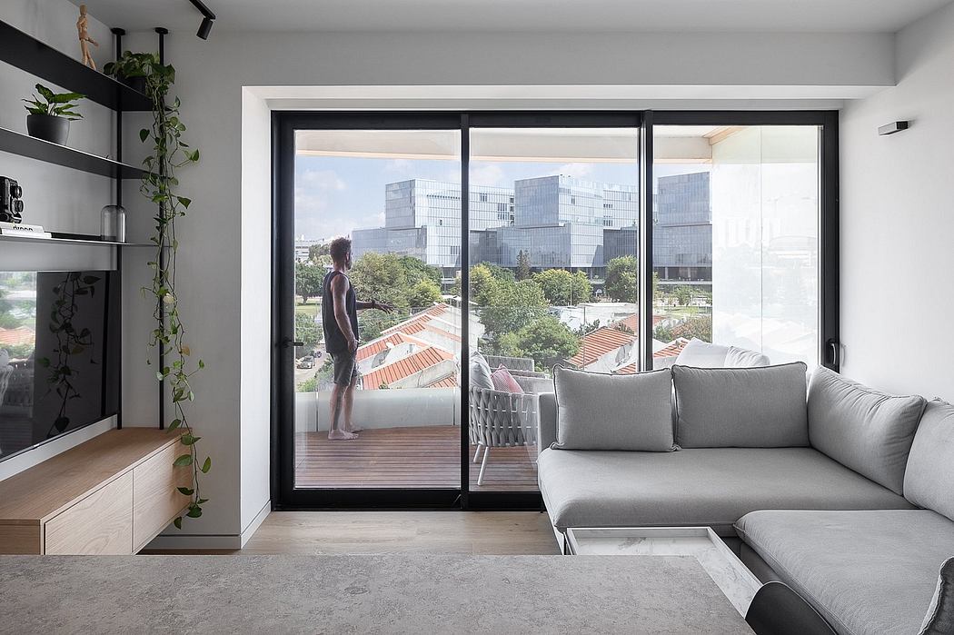 Modern loft-style apartment with large glass windows, grey sofa, and city skyline view.