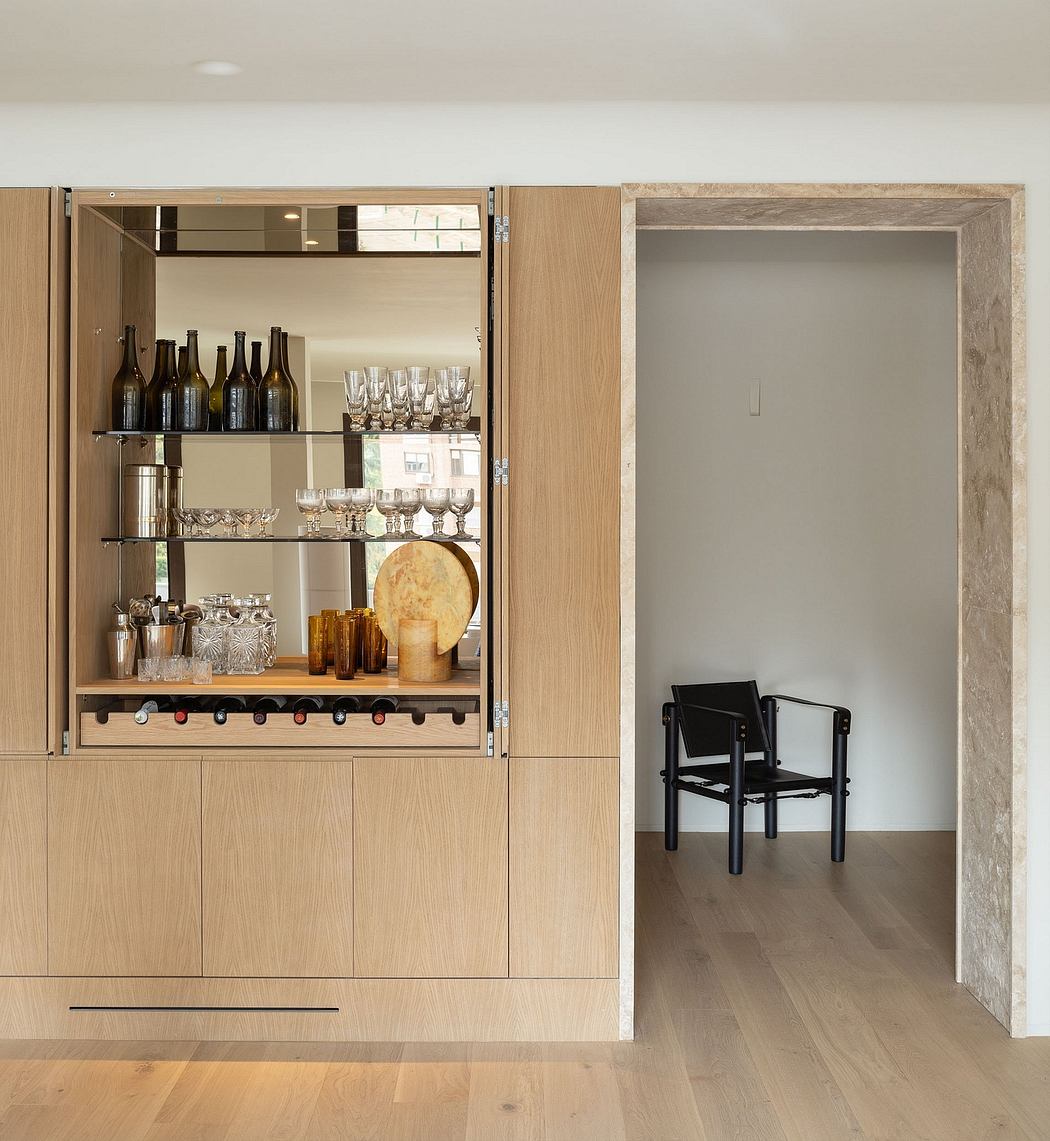Built-in wooden shelving unit with glassware, bottles, and a chair in the adjacent room.