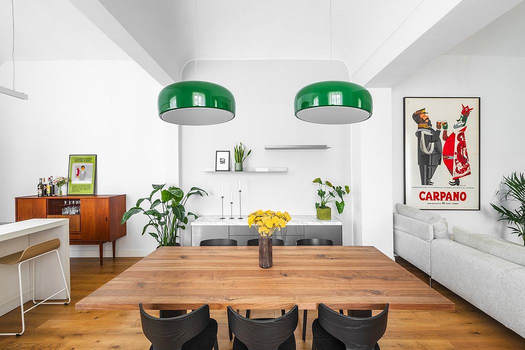 Bright, minimalist dining space with wooden table, hanging green lamps, and framed artwork.