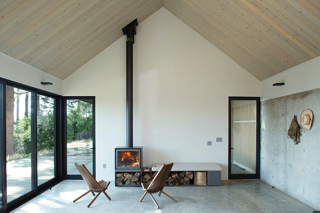 A cozy cabin interior with large windows, rustic wood ceiling, and a central fireplace.