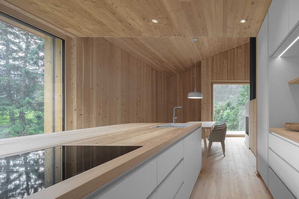 A modern, minimalist kitchen with a wooden interior and large windows overlooking nature.