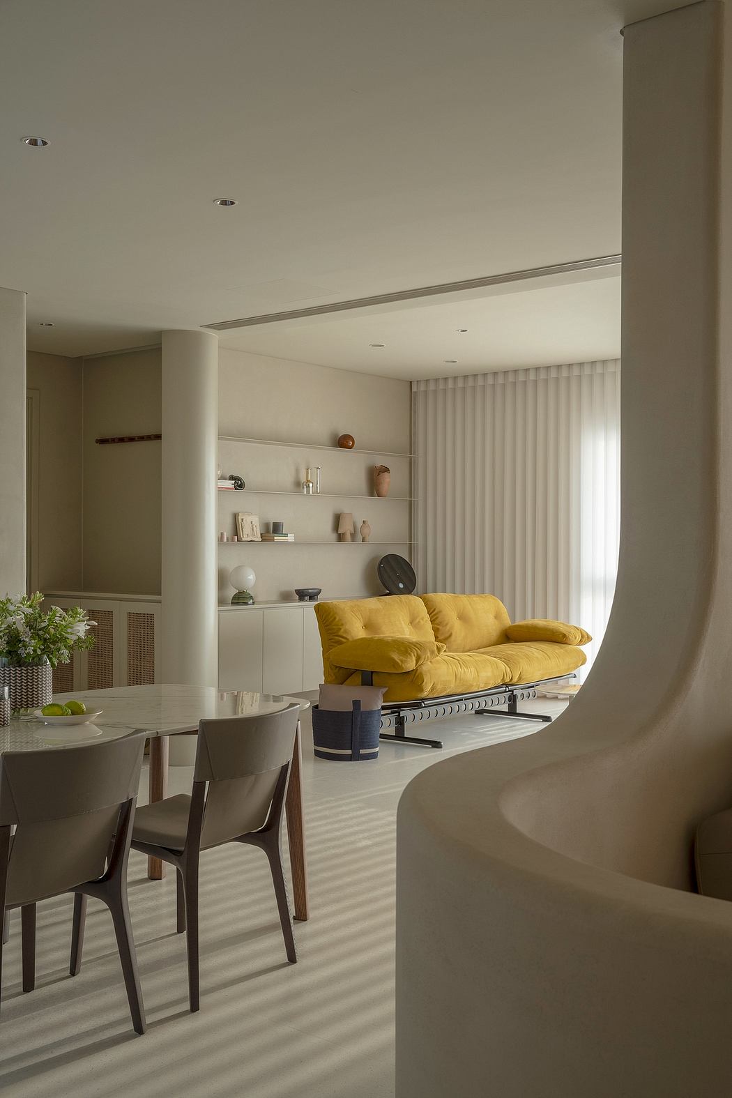 Modern, minimalist living room with yellow couch, built-in shelving, and dining area.