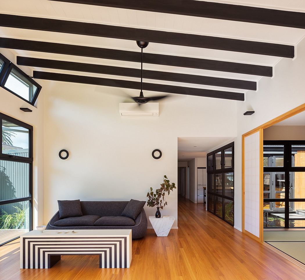 Modern open-plan living space with black exposed beams, wood flooring, and sleek furnishings.
