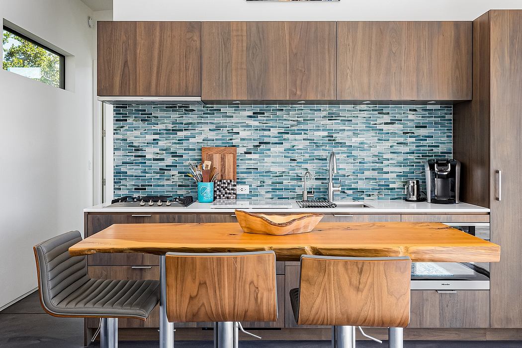 Modern kitchen with wood cabinetry, sleek tile backsplash, and a large wooden dining table.