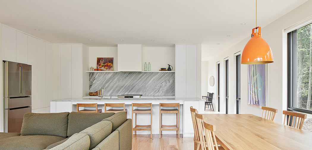 A modern, open-concept kitchen and dining area with white cabinetry, sleek marble countertops, and natural wood furnishings.