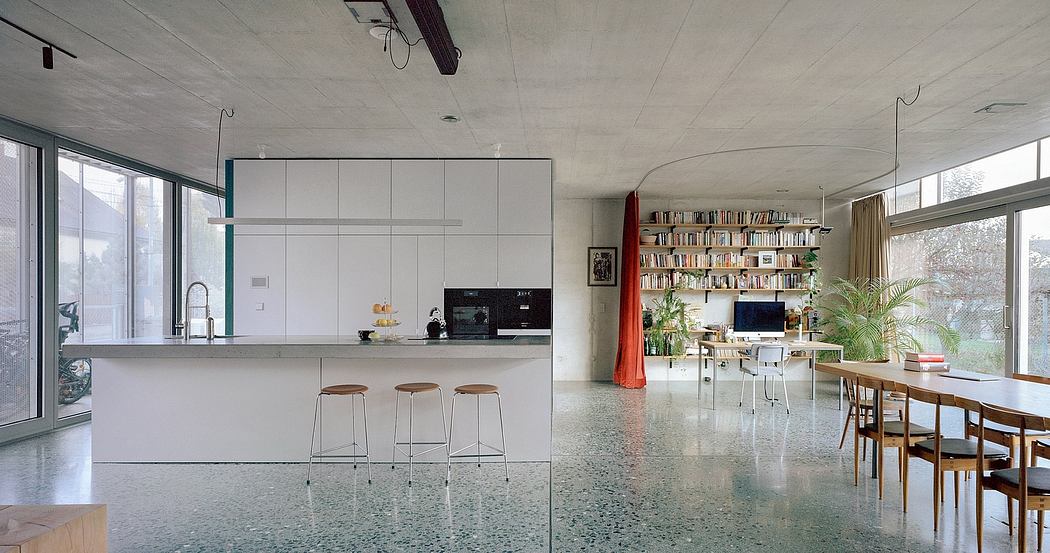 Spacious, minimalist kitchen and dining area with concrete floors, built-in shelves, and large windows.