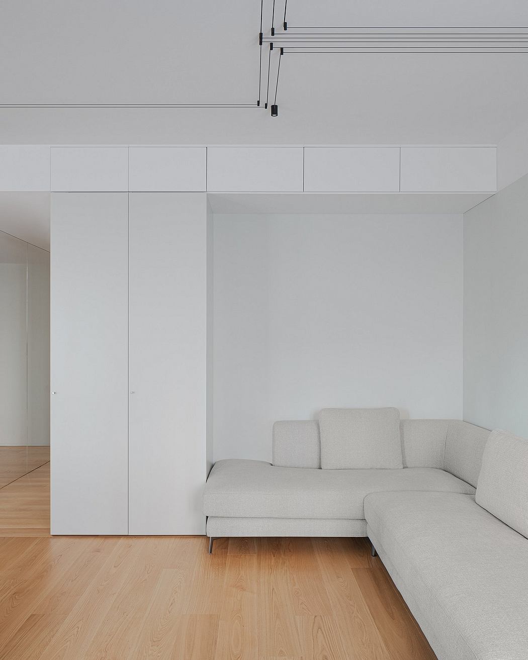 Modern, minimalist living room with built-in storage, wood floor, and gray sectional sofa.