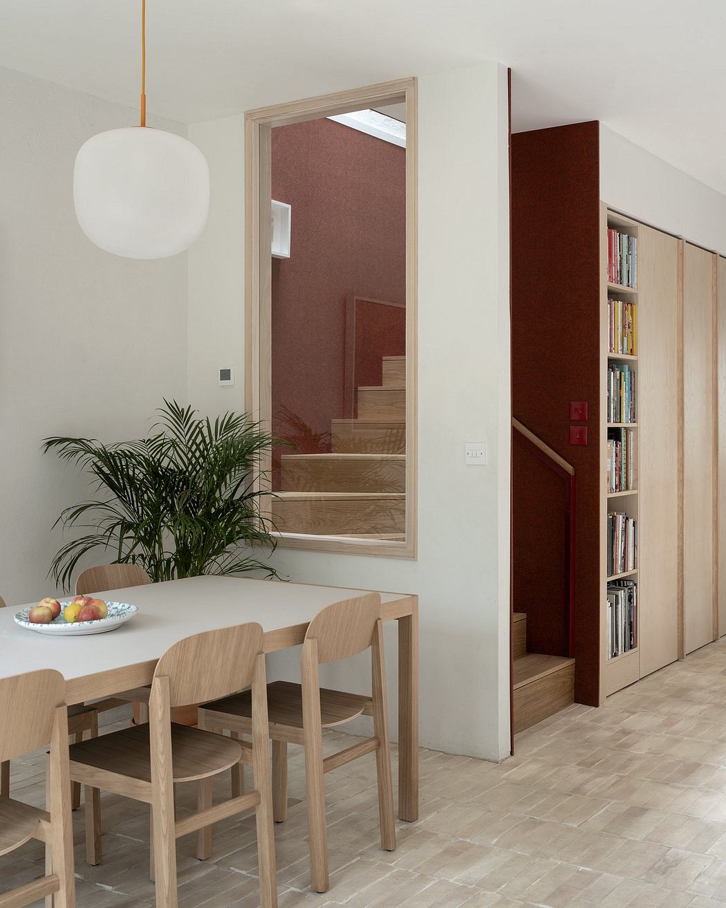 A modern dining area with wood furnishings, a built-in bookshelf, and a white pendant lamp.