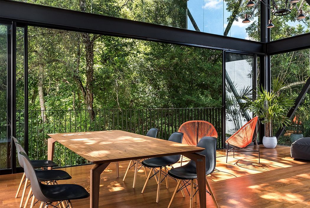 A modern, glass-enclosed dining area with a wooden table, black chairs, and lush greenery outside.