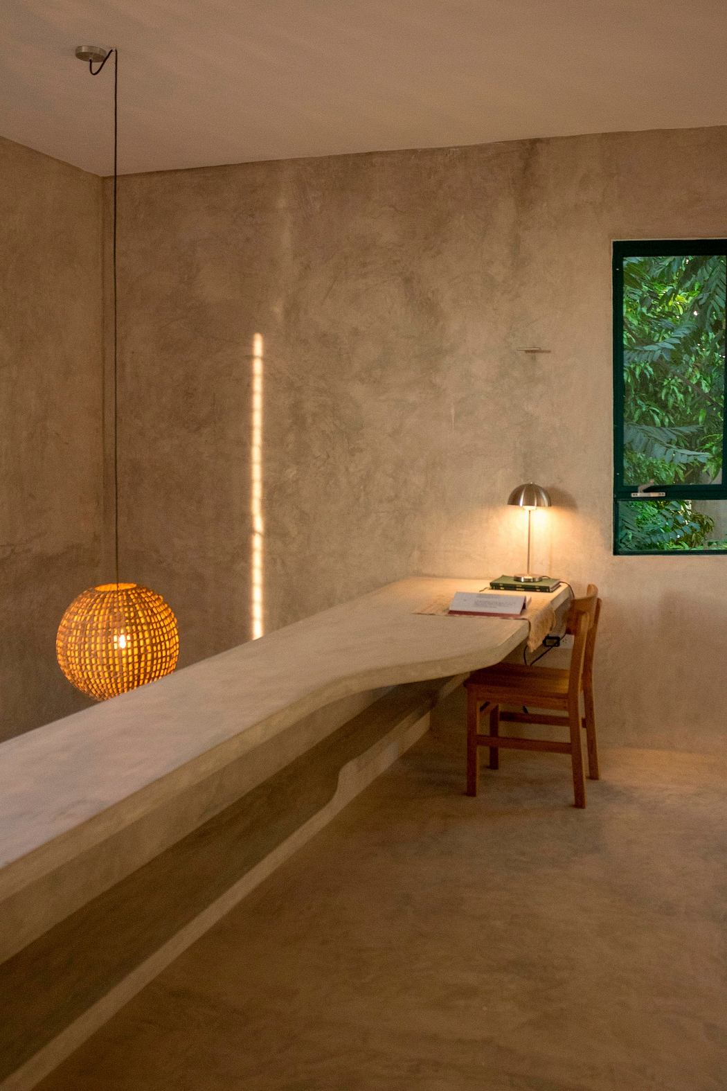 A cozy, minimalist workspace with a wooden desk, lamp, and woven pendant light against a textured wall.