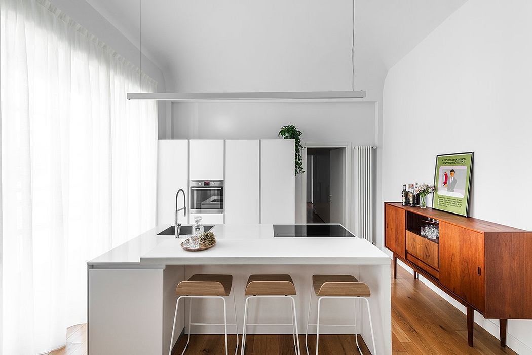 A modern, minimalist kitchen with a sleek white island, wooden accents, and pendant lighting.