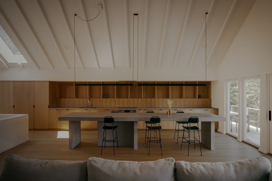 Modern kitchen with wooden cabinets, concrete countertop, and pendant lights in a bright, airy space.