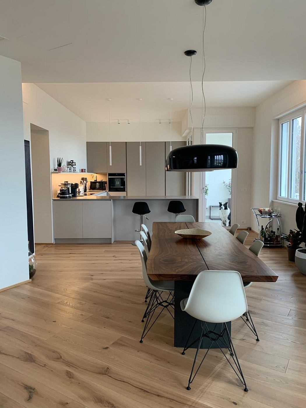 Spacious open-plan kitchen and dining area with modern gray cabinets, wooden table, and stylish lighting.
