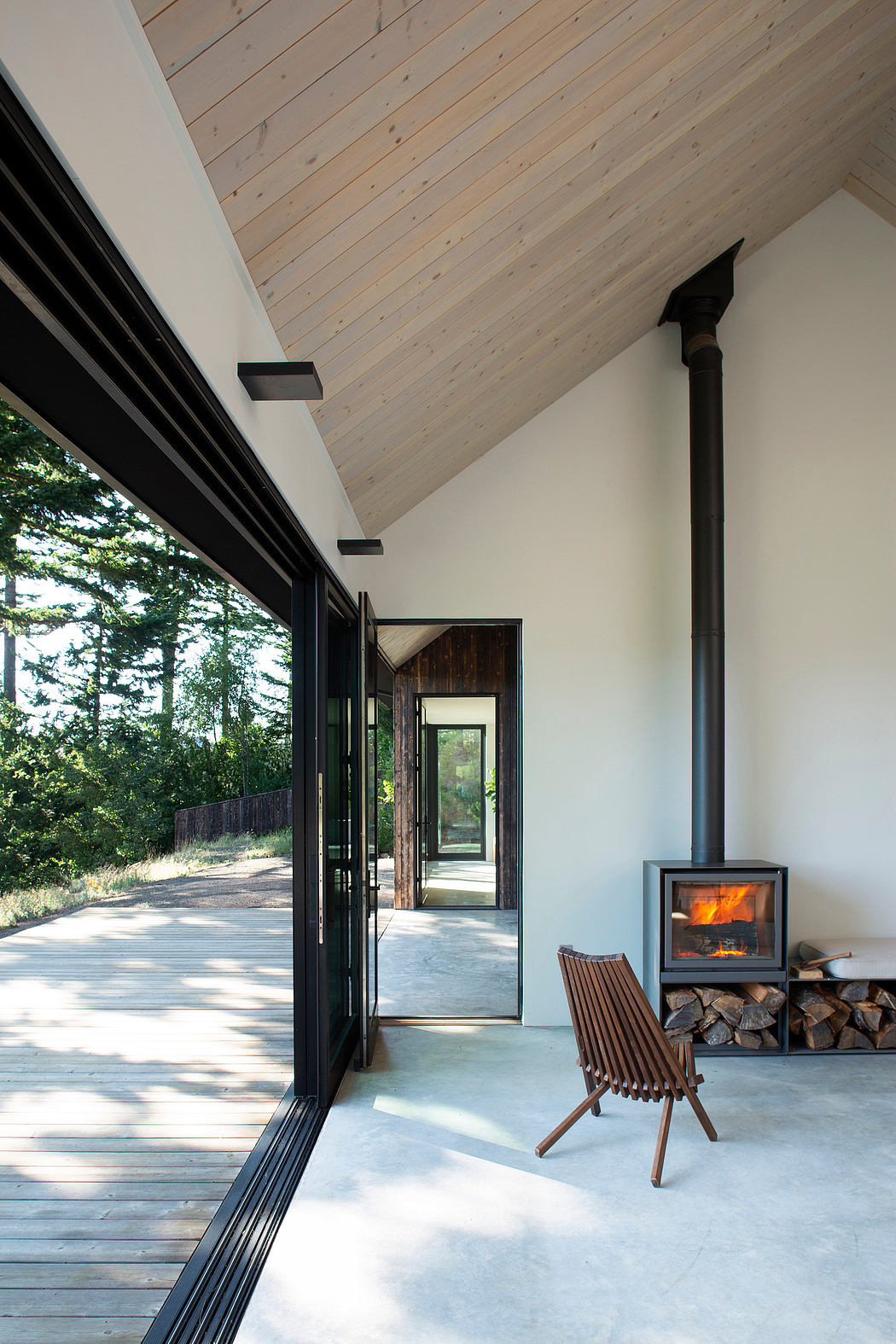 Inviting wood-paneled interior with a cozy fireplace, glass walls, and a rustic bench.
