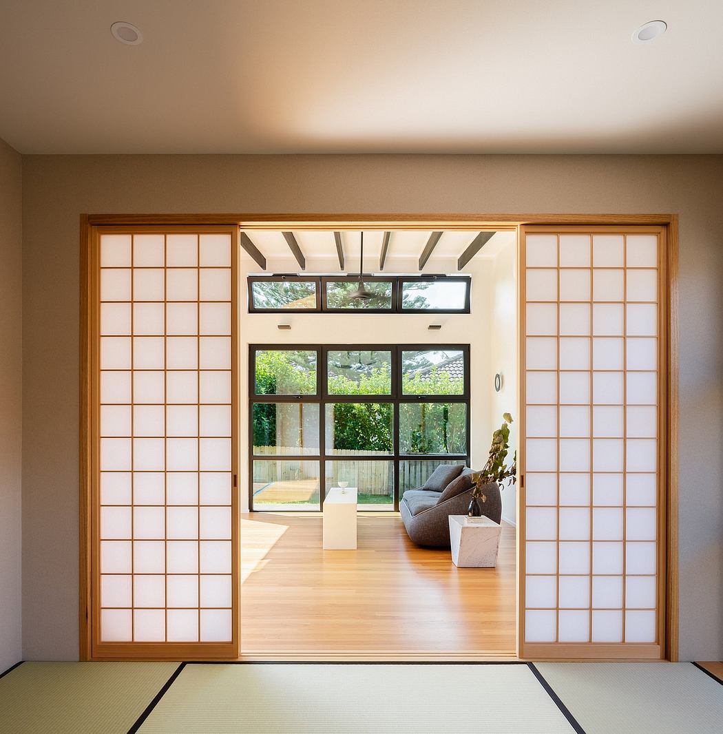 A spacious room with minimalistic Japanese-style sliding doors, wooden floors, and large windows overlooking a lush garden.