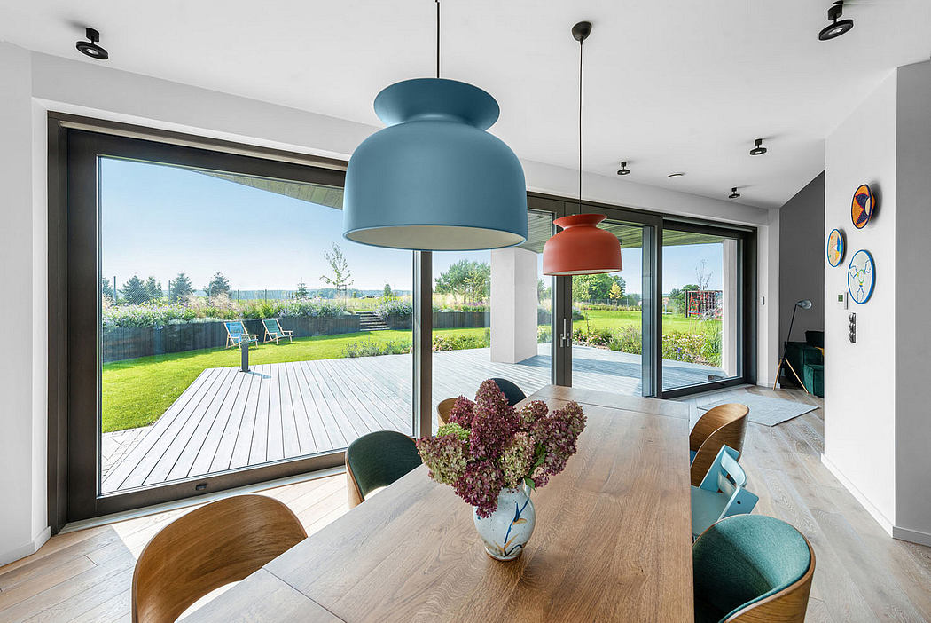 Modern dining room with large windows, wooden table, colorful pendant lights, and outdoor deck.