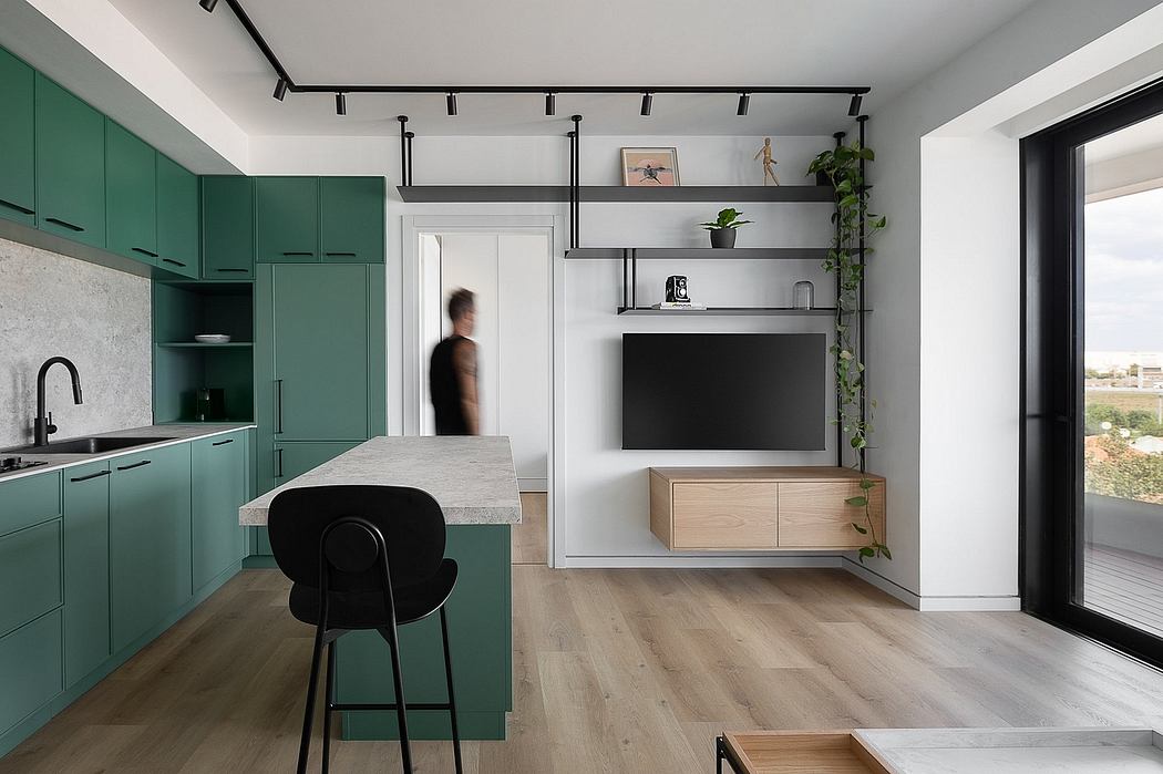 Modern, open-plan kitchen with muted green cabinets, sleek black fixtures, and floating shelves.
