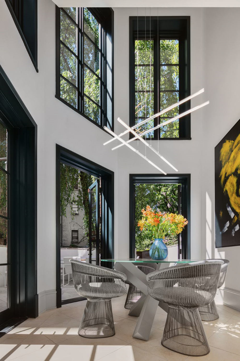 Sleek, modern dining area with black-framed windows, wire-frame chairs, and hanging light fixtures.