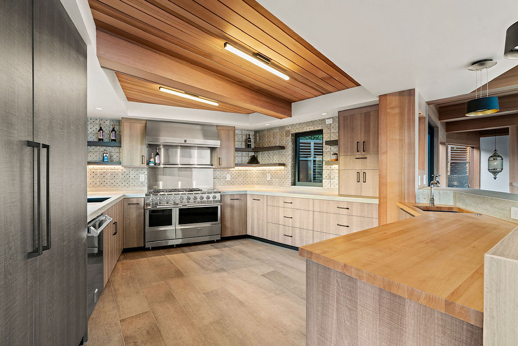 A modern kitchen with wood-paneled ceiling, stainless steel appliances, and a large central island.