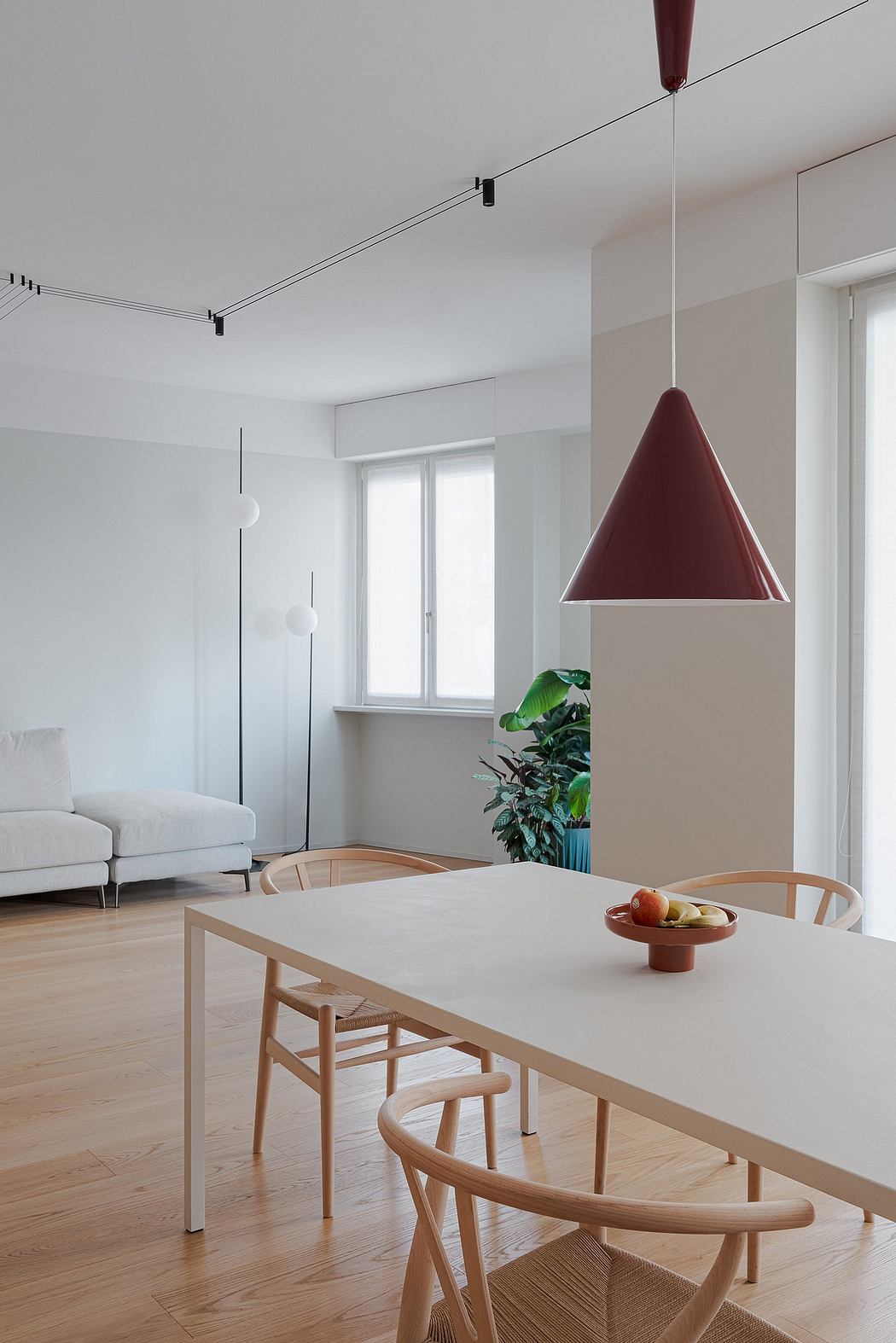 Modern dining area with minimalist furniture, pendant light, and lush plant.