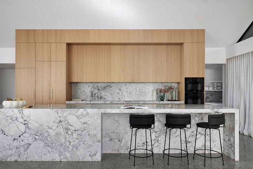 Sleek, modern kitchen with wood cabinets, marble countertops, and minimalist bar stools.