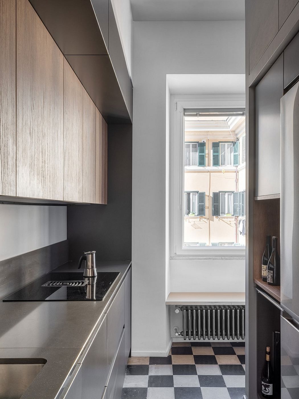 Sleek kitchen design with black countertop and wooden cabinetry, leading to a hallway with a checkered floor.