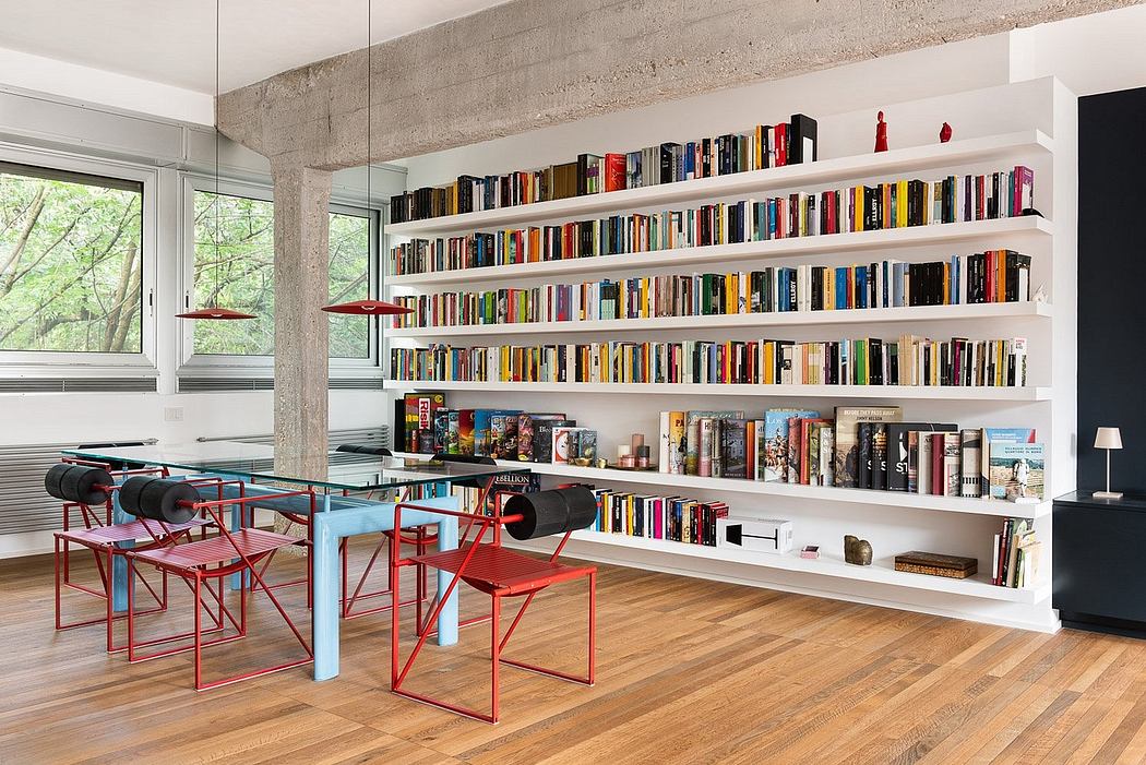 Spacious open-plan room with concrete ceiling, built-in bookshelves, and colorful chairs.