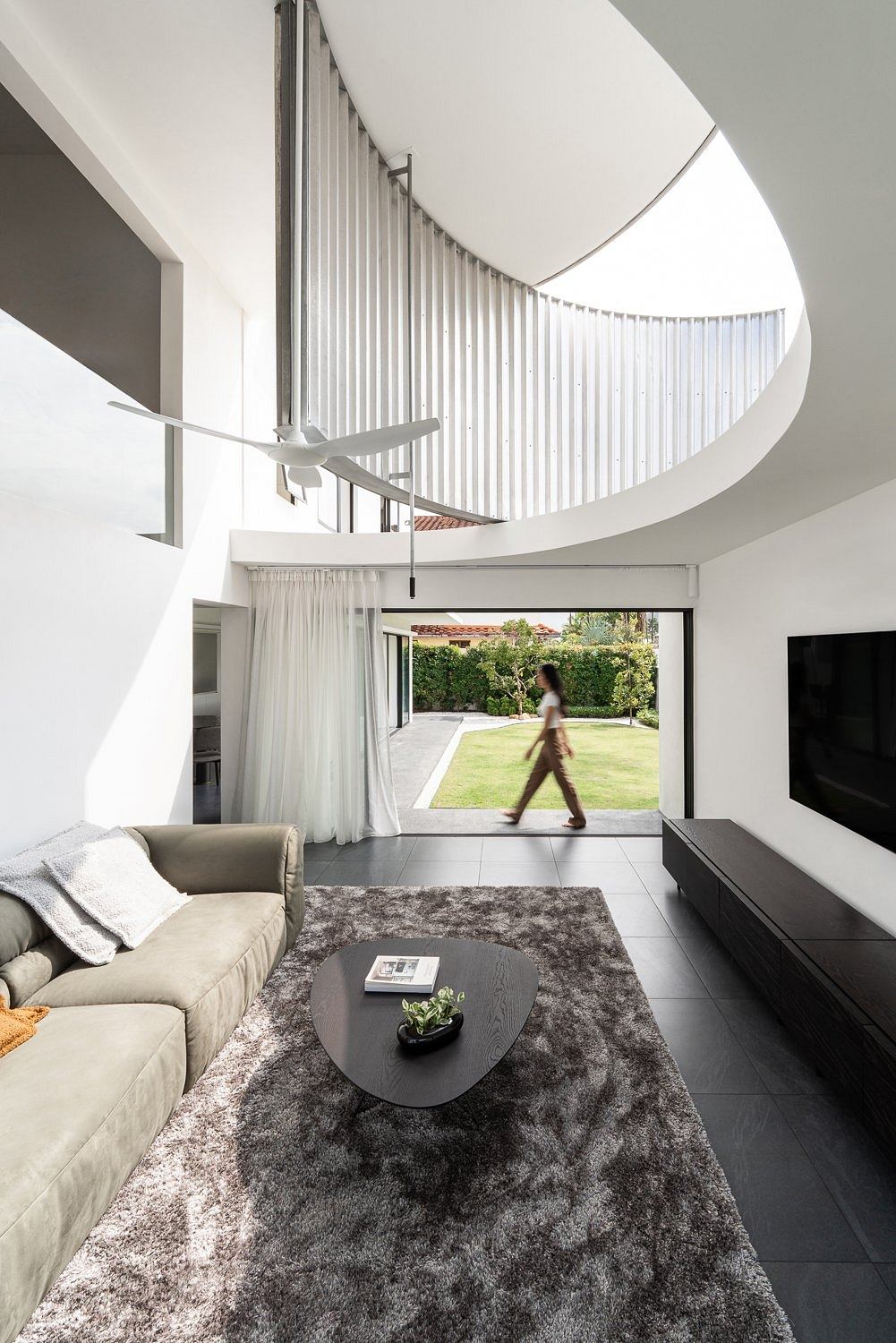 Curved staircase with metallic railing in contemporary living room with garden view.