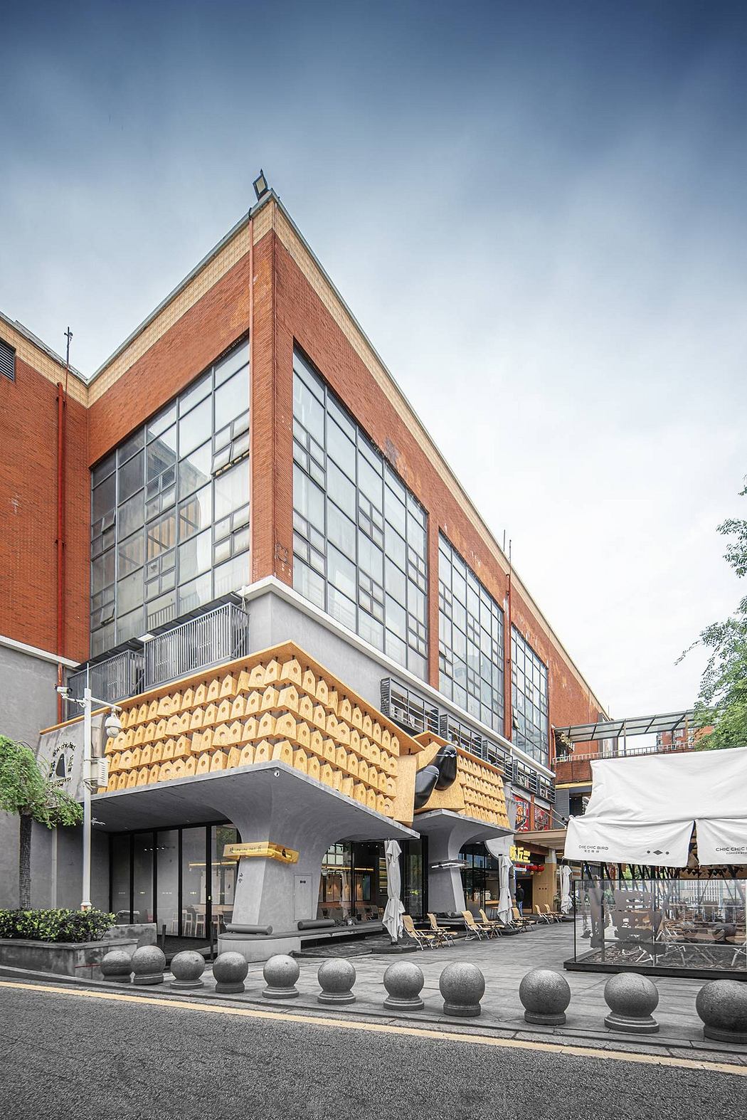 A modern, glass-walled building with a distinctive brick façade and an elevated outdoor seating area.
