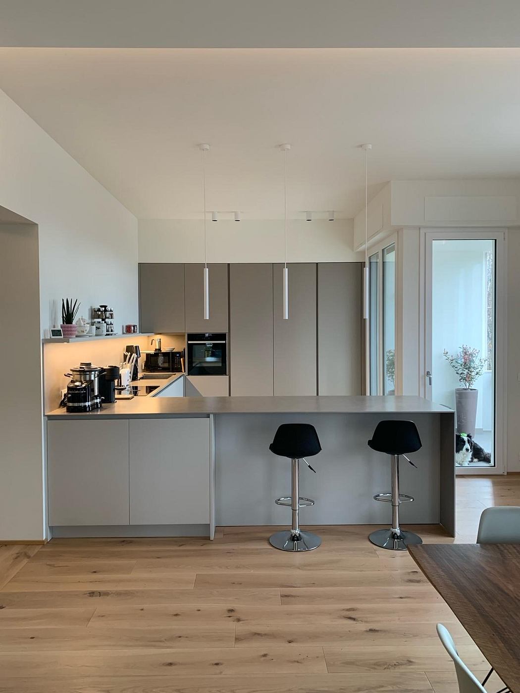 A modern kitchen with sleek gray cabinets, wood floors, and adjustable black stools.