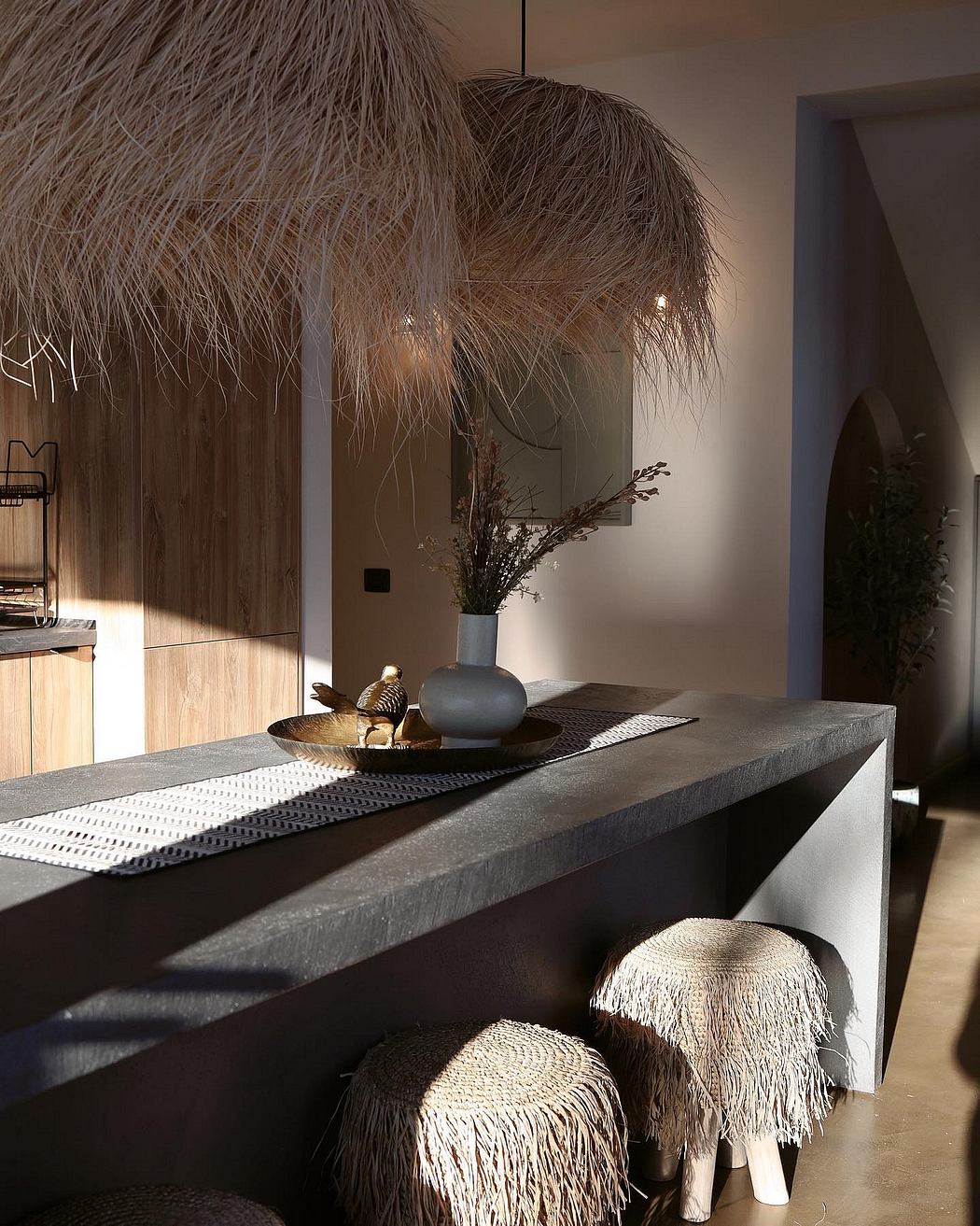 Minimalist, textured interior with pendant light, decorative vase, and sculptural stools.